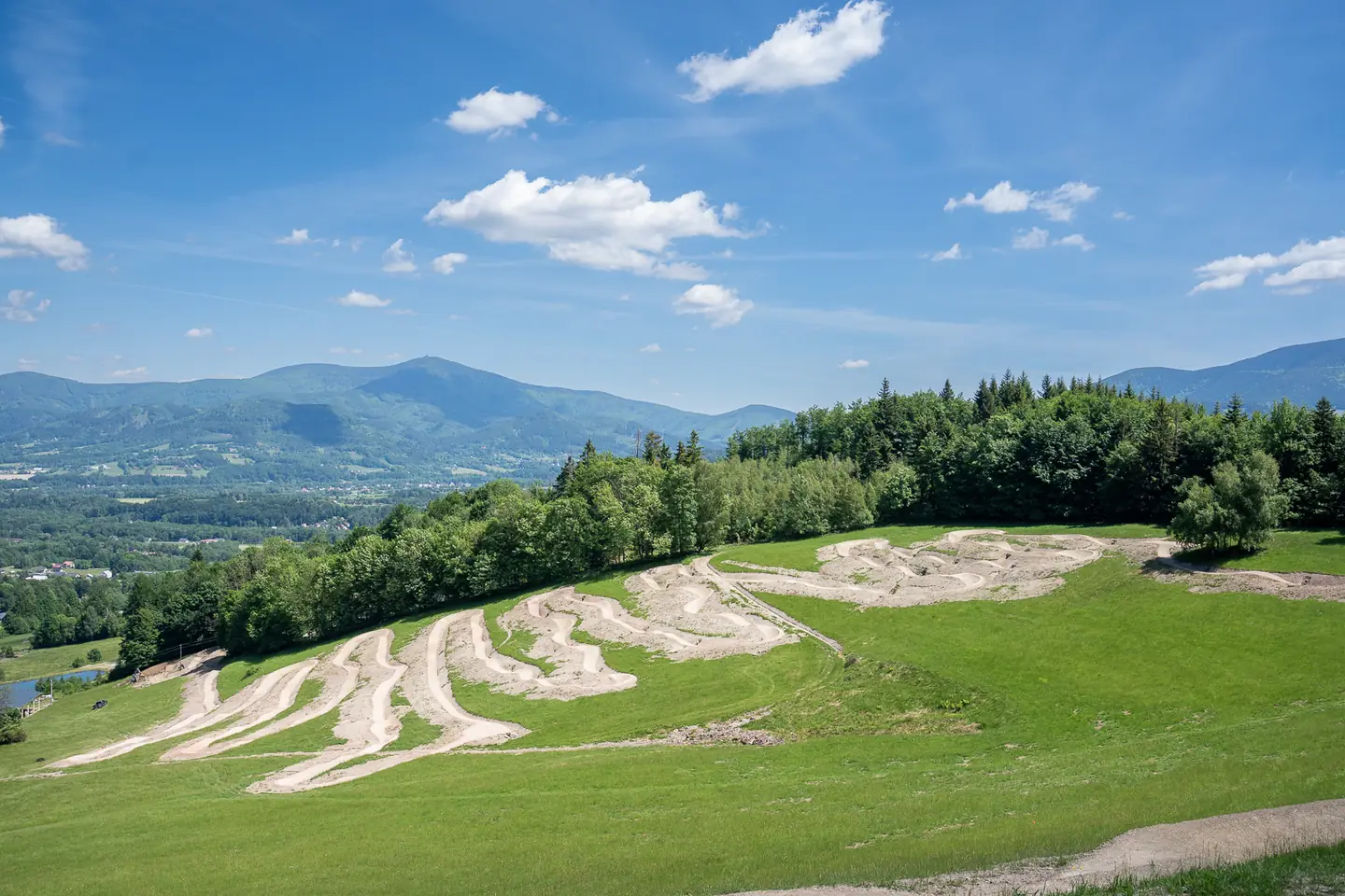Letecký pohled na tratě bikeparku Opálená na zeleném svahu nad panoramatem Beskyd